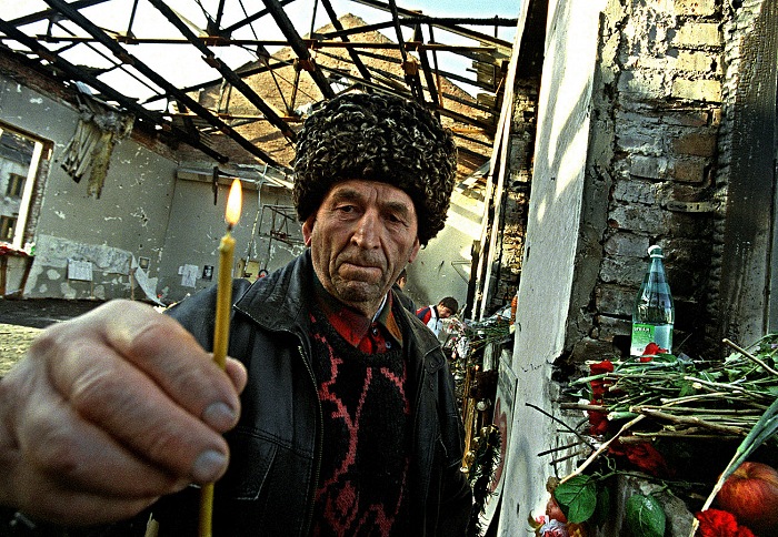 Beslan, Ossezia,Caucaso, 4 settembre 2004. Un anziano abitante di Beslan, nonno di una delle giovani vittime, depone candele tra le macerie della palestra della Scuola 1 dov' avvenuto il sanguinoso attacco dei guerriglieri ceceni. Nello scontro a fuoco con le le truppe speciali russe morirono 333 civili di cui 198 bambini, 738 furono i feriti e i mutilati. Questa foto venne scattata il giorno dopo la fine dei combattimenti, quando la stampa fu autorizzata a entrare nell'edificio dopo la bonifica degli ordigni inesplosi.  Livio Senigalliesi.