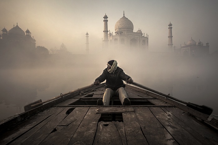 Bruno Tamiozzo, Un uomo, attraversa con la sua barca, il sacro fiume Yamuna, che scorre alle spalle del grande Taj Mahal, Agra, Uttar Pradesh, India, 2013.  Bruno Tamiozzo.