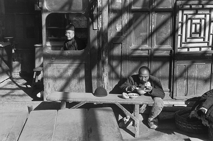Henri Cartier-Bresson, Un cameriere siede alla finestra aperta di una taverna, mentre un coolie mangia allesterno sotto una pergola. Pechino, dicembre 1948, Gelatin silver print, 1957.  Fondation Henri Cartier-Bresson / Magnum Photos.