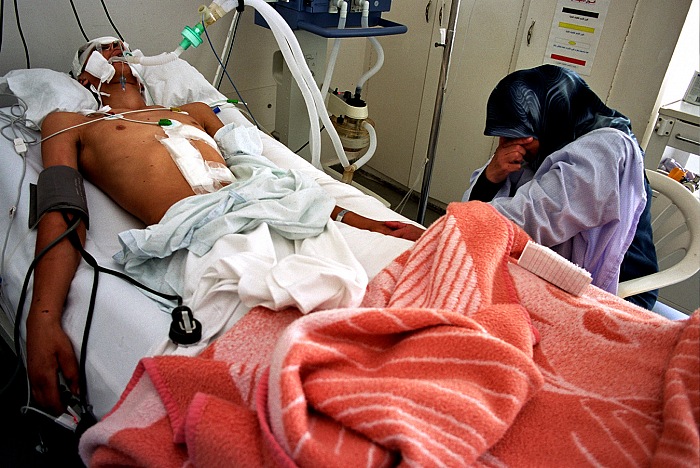 Tyr, Sud Libano, 2006. Reparto rianimazione Ospedale Jabal Amel. Hussein Ali Kdouh, 17 anni, giace in fin di vita, vittima di una cluster bomb. L'ordigno l'ha colpito mentre cercava di rimuovere le macerie della casa distrutta dai raid aerei israeliani. Al suo capezzale la madre Mariam piange disperata e legge brani del Corano. La foto è stata scattata nei pressi della zona di confrontazione tra guerriglieri Hezbollah ed Esercito israeliano. Tra il luglio e l’agosto del 2006 trascorsi 45 giorni in prima linea. © Livio Senigalliesi.